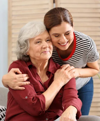 A smiling younger woman hugs an older woman with silver hair from behind